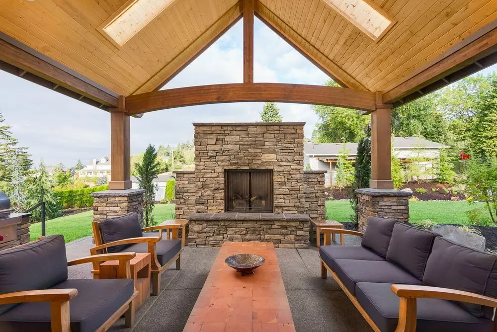 Cedar gable patio cover with a stone fireplace and outdoor sofa seating