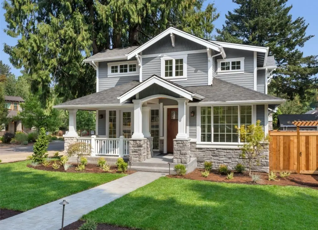 Gray Craftsman house with porch, stone accents, and green lawn on a sunny day.