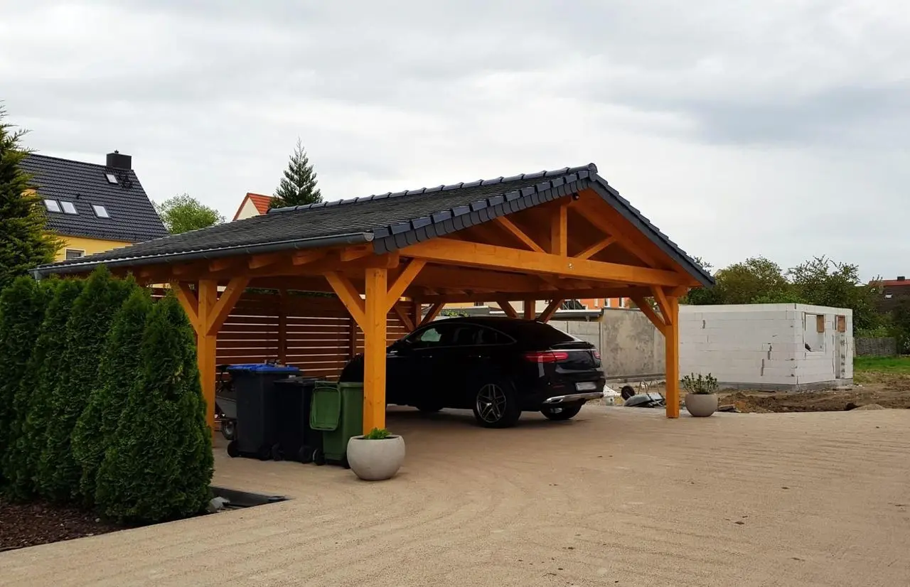 Freestanding timber carport with a dark roof covering a car on a gravel driveway
