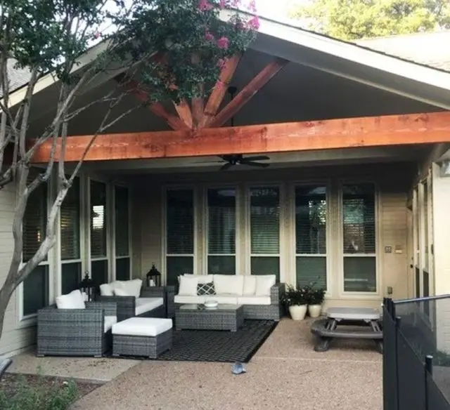 Patio with outdoor seating under a covered area with a wooden beam and a tree.
