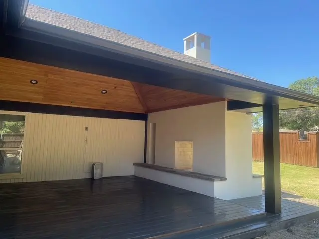 Covered deck with dark-stained flooring and a built-in outdoor fireplace wall