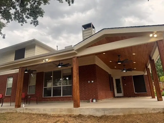 Wide cedar patio cover with recessed lights extending across a brick home