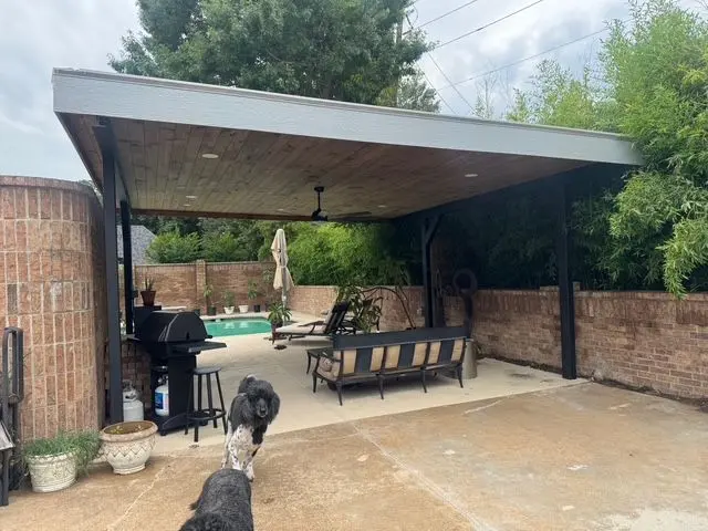 Flat-roof patio cover shading a backyard grill and lounge area