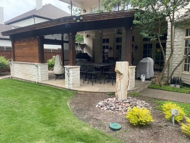 Covered patio with stone column bases and a dining set beside a landscaped lawn