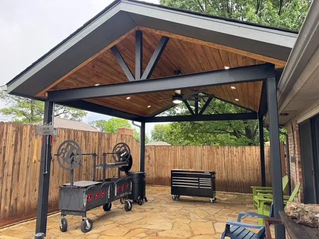 Freestanding pavilion with dark steel posts over a flagstone patio and smoker
