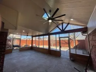 Screen room interior with a gable ceiling, large fan, and backyard view