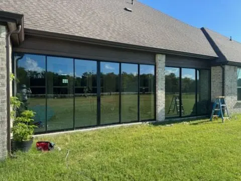 Black-framed glass wall enclosure across the back of a brick home