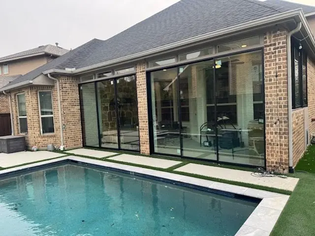 Black-framed glass sunroom walls overlooking a backyard pool