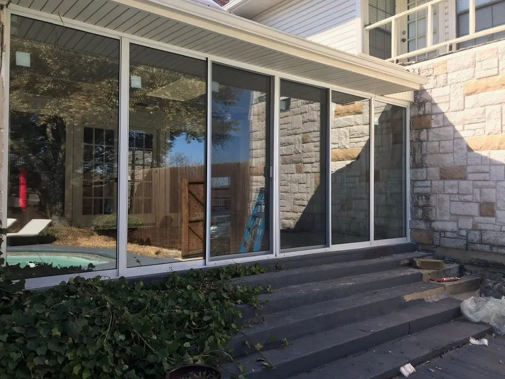 Glass sunroom enclosure on a stone home with steps down to the yard