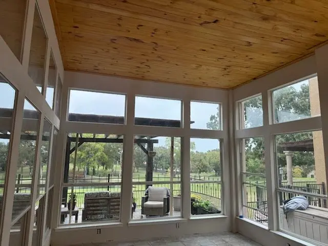 Sunroom interior with wraparound windows and a pine plank ceiling